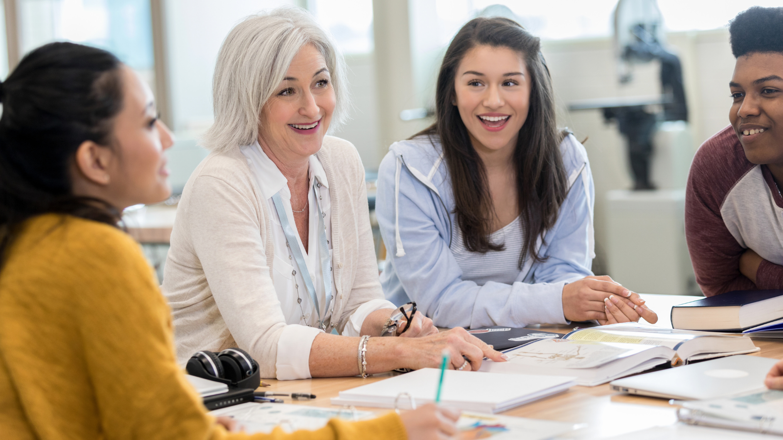 A faculty member sits with students around a table, smiling and engaged in discussion—representing trauma-informed, relational learning at the Becoming Institute.