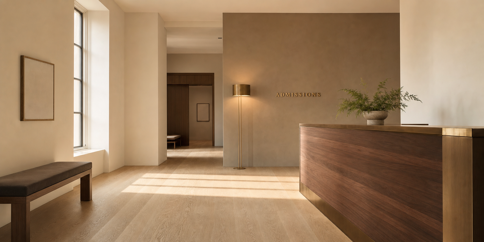 Architectural interior of the Becoming Institute admissions threshold — warm afternoon light, walnut and brass reception desk, cream walls
